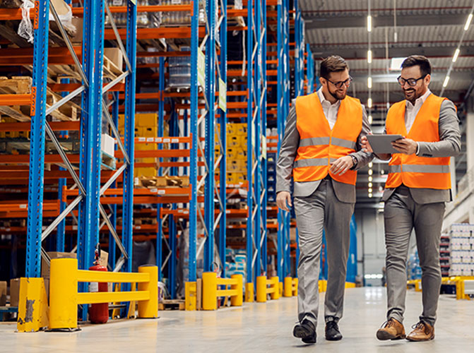 Two guys walking in warehousing looking at ipad